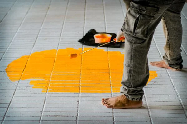 Barefoot individual painting a yellow circle on white tiles using a roller brush, focusing on creativity.