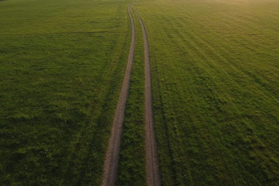 Aerial drone photo of a large open green field with a dirt path