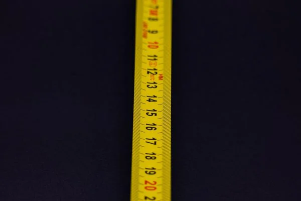 Detailed shot of a yellow measuring tape with numbers on a dark background.